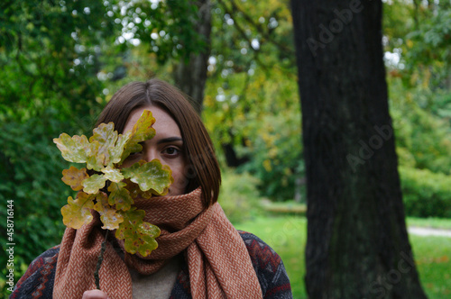 beautiful young woman with red hair holding autumn leaves by her face in the park in autumn. High quality photo