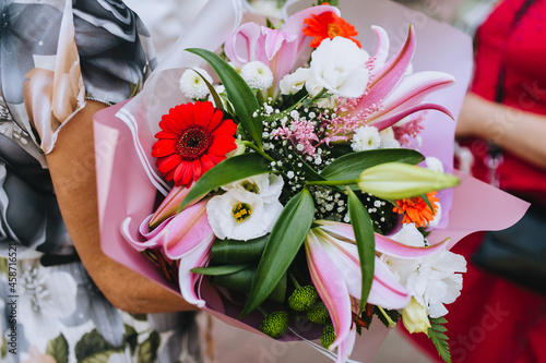 A bouquet of beautiful flowers in a pink paper package in the hands of a woman close-up. Wedding photography, gift.