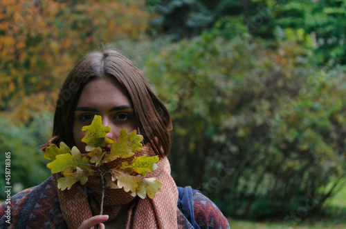 beautiful young woman with red hair holding autumn leaves by her face in the park in autumn. High quality photo