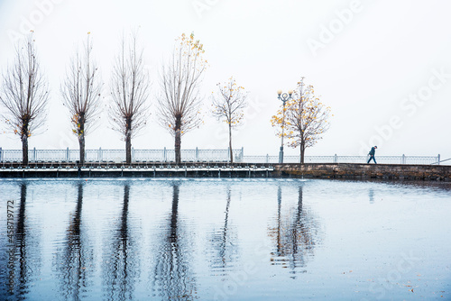 Obraz na płótnie Mystical spooky depressing autumn landscape with a silhouette of a passerby and trees with yellow leaves on a background of fog over the lake. (Autumn depression, sadness, psychotherapy - concept) w salonie