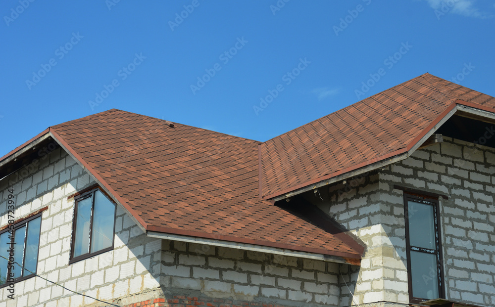 An asphalt-shingled roof valley as a top roofing problem area of a new house built from concrete blocks. A close-up of a brown asphalt shingled roof with a closed valley.