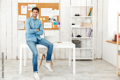 Young brunette man smiling while sitting on desk in office © Drobot Dean
