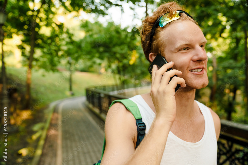 Ginger sportsman smiling while talking on mobile phone in park Ginger sportsman smiling while talking on mobile phone in park