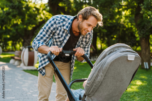 White father smiling while walking with her son in baby carriage at park