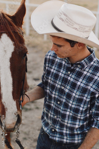 Fényképezés Vertical closeup shot of a young cowboy holding his horse