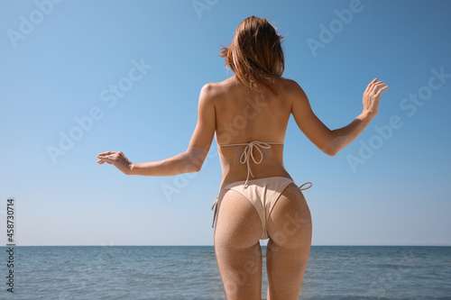 Woman with sand on perfect body in bikini near sea, back view
