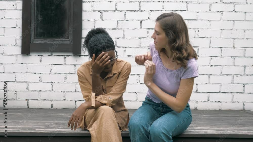 Young lonely african sad woman crying and her caucasian friend supporting her. Friend helping with depression, anxiety and sadness Young lonely african sad woman crying and her caucasian friend supporting her. Friend helping with depression, anxiety and sadness