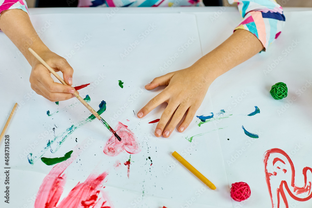 Cute child sitting at the table and drawing red heart on white paper Cute child sitting at the table and drawing red heart on white paper