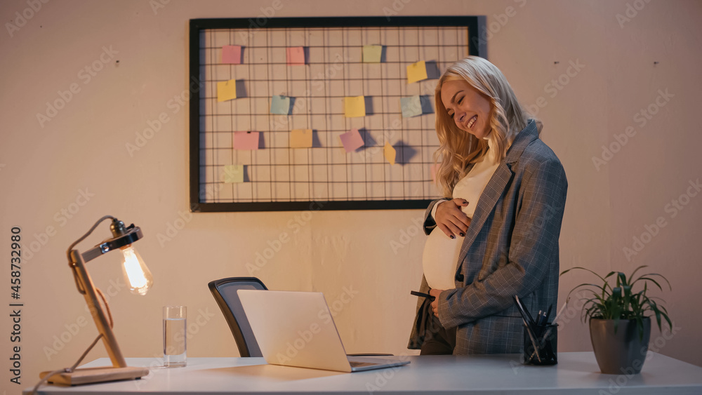 Smiling pregnant businesswoman having video call on laptop in office in evening Smiling pregnant businesswoman having video call on laptop in office in evening