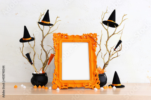 holidays image of Halloween. witcher cauldron and hat, broom, bare trees, photo frame over white wooden table photo