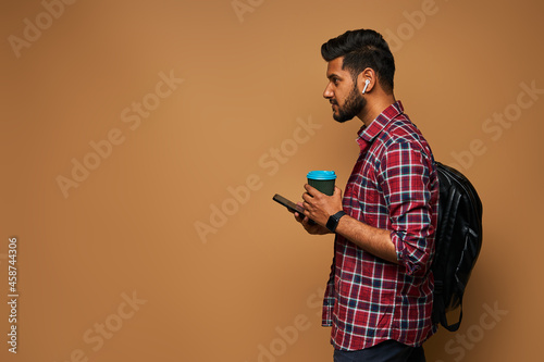 Handsome indian man in casual close with coffe to go and backpack on pastel background copy space
