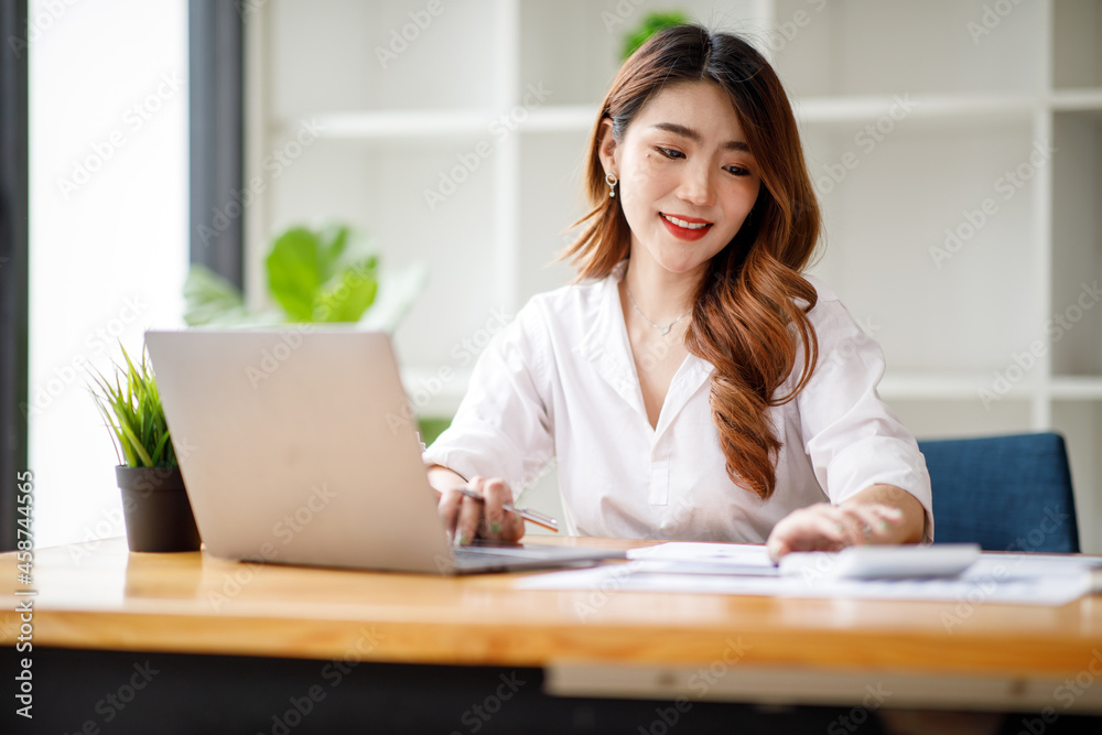 Young Asian businesswoman beautiful charming smiling and working with a computer laptop in the office. doing Financial analysis reports the graph of the company's and growth Market research. Young Asian businesswoman beautiful charming smiling and working with a computer laptop in the office. doing Financial analysis reports the graph of the company's and growth Market research.