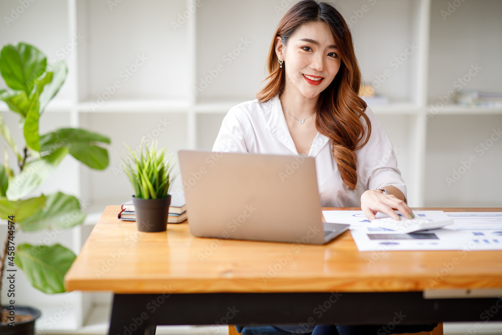 Young Asian businesswoman beautiful charming smiling and working with a computer laptop in the office. doing Financial analysis reports the graph of the company's and growth Market research. Young Asian businesswoman beautiful charming smiling and working with a computer laptop in the office. doing Financial analysis reports the graph of the company's and growth Market research.