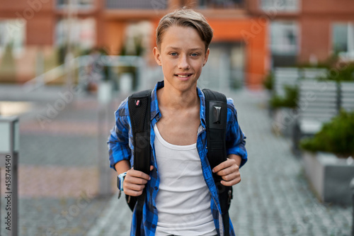 Portrait of little pupil boy with backpack near school
