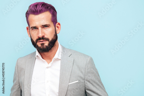 Portrait of handsome confident stylish hipster lambersexual model.Sexy modern man dressed in elegant suit. Fashion male posing in studio near blue wall. With pink hair