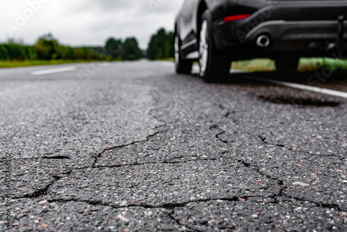 Broken asphalt on the background of parking car on the road. © Natallia