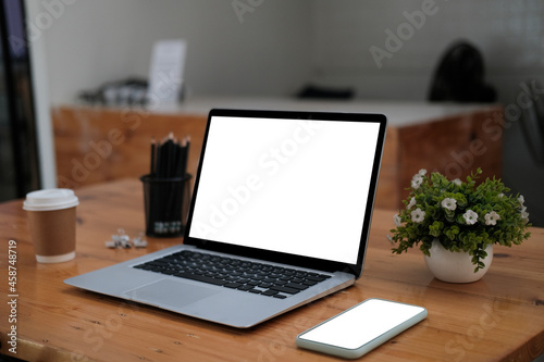 Photo of white screen computer laptop on a wooden table surrounded by personal equipment.