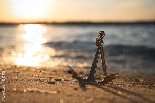 Metal anchor on shore near river at sunset