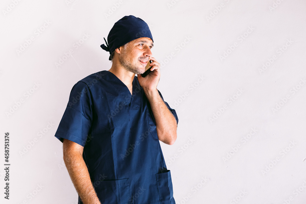 Male nurse, doctor or veterinarian in blue uniform at a window in a hospital, talking on the mobile phone. Medicine, hospital and healthcare concept.