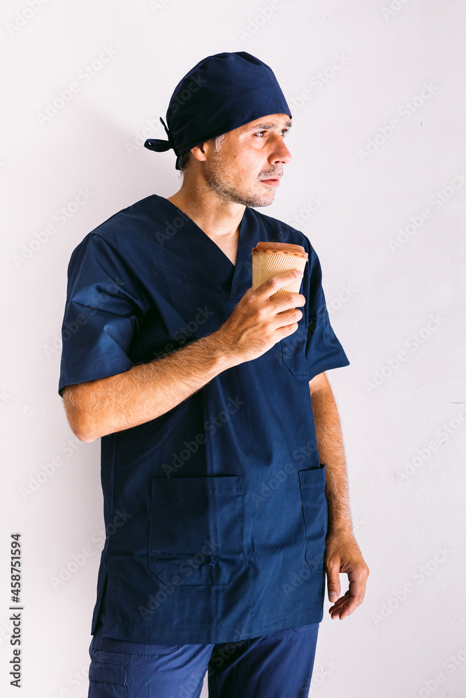Male nurse, doctor or vet in dark blue uniform looking out of a window in a hospital, having coffee: Medicine, hospital and healthcare concept. Male nurse, doctor or vet in dark blue uniform looking out of a window in a hospital, having coffee: Medicine, hospital and healthcare concept.