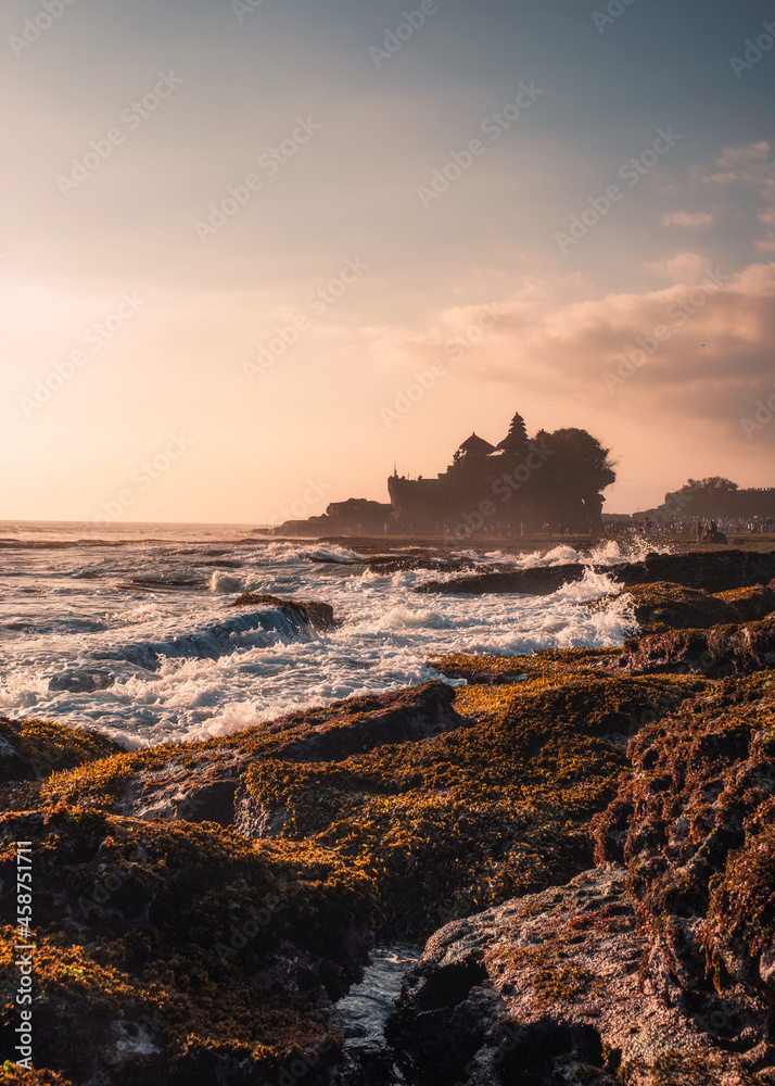 Pura Tanah Lot temple on clifftop and wave hitting on sunset beach in Bali