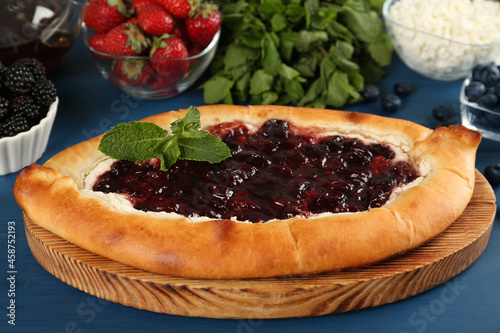 Delicious sweet cottage cheese pastry with cherry jam and fresh berries on blue wooden table, closeup