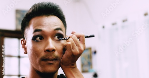 A charming short-haired Asian gay who owns a small beauty salon in the village is writing his eyeliner as he uses his mobile phone to record a video to post on social media.