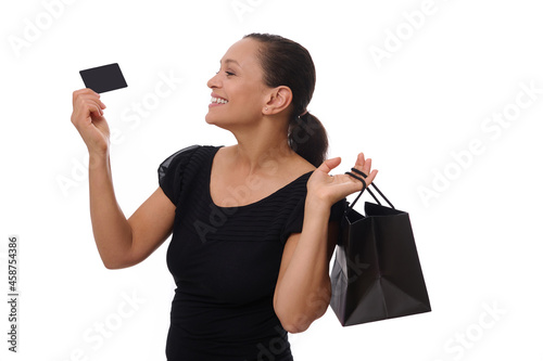 Portrait of young mixed race African American woman smiling with beautiful toothy smile holding shopping bags and credit or discount card in hands, standing against white background with copy space