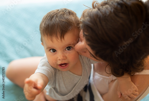 Close up portrait of a mother hugging and kissing her baby while baby is pointing and looking up. Family lifestyle. 