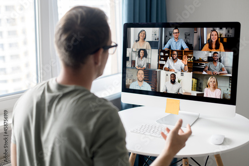View from back above male shoulder on the laptop with diverse employees, coworkers on the screen, video call, online meeting. App for video conference with many people together photo