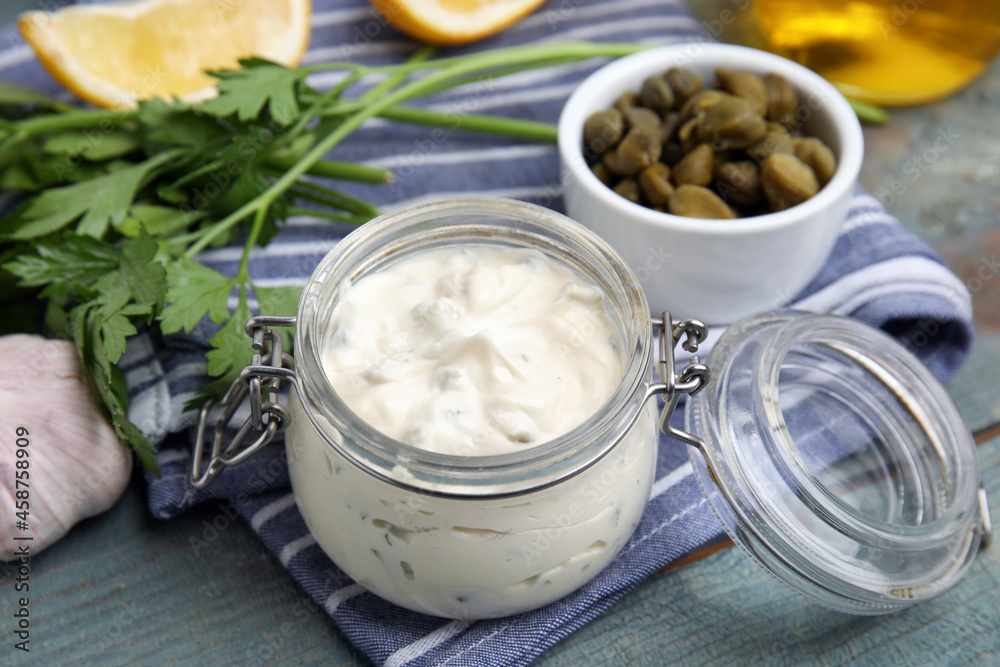 Tasty tartar sauce in glass jar and ingredients on light blue wooden table Tasty tartar sauce in glass jar and ingredients on light blue wooden table