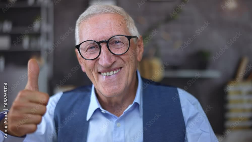 Portrait closeup of a happy self-confident attractive old businessman with black eyeglasses looks at the camera and gives thumbs up as a sign of success and wellness.