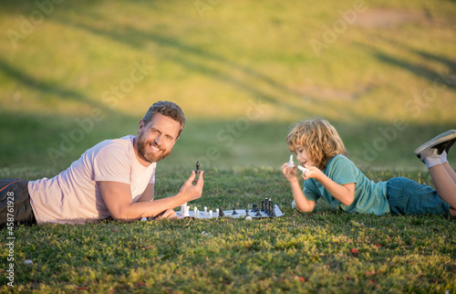 friendship. dad and kid play logic game. father and son playing chess on grass in park.