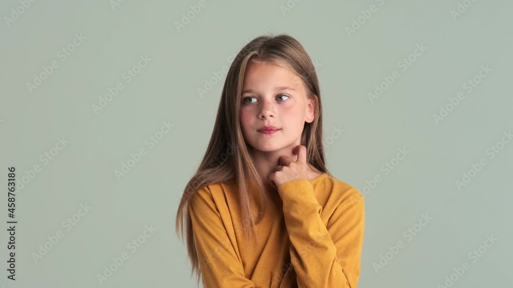 A small beautiful girl pondering standing isolated over gray wall in the studio A small beautiful girl pondering standing isolated over gray wall in the studio