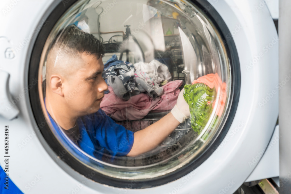 View through the door of a washing machine of a man taking out clothes View through the door of a washing machine of a man taking out clothes
