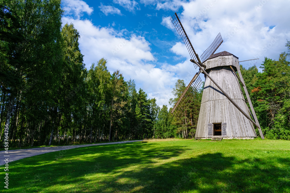 Obraz premium Old wooden windmill over meadow and cloudy sky.