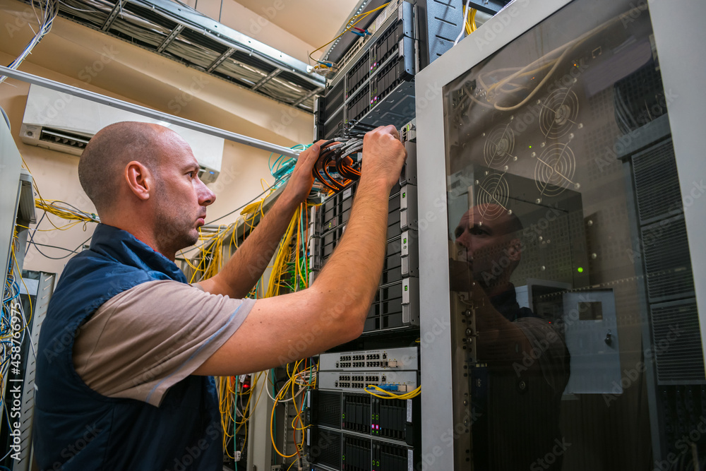 An engineer connects the fiber optic cable to the switch's network interface. A man works in a data center server rack. Maintenance of computer equipment of an Internet provider.