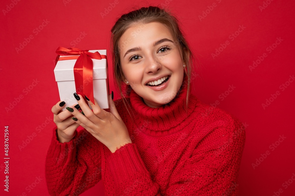Naklejka premium Shot of attractive positive smiling young brunette woman isolated over colourful background wall wearing everyday trendy outfit holding gift box and looking at camera