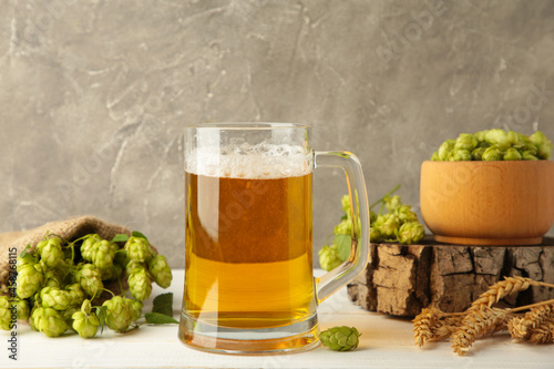 Glass of fresh beer with green hops and wheat on a grey background