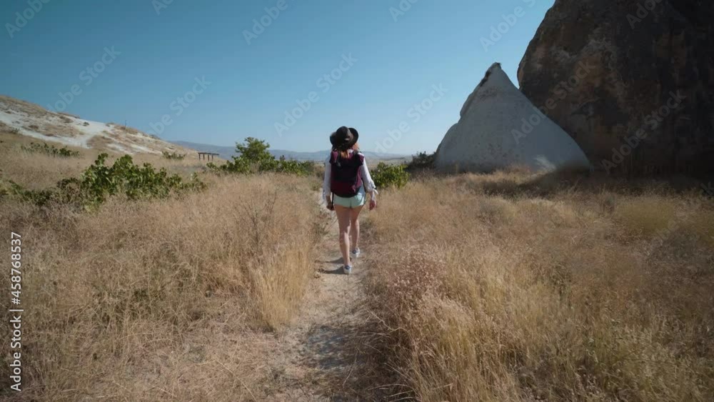 Traveler girl walking, back view with backpack and leather hat, tourist. Fairy chimneys park in the background. rock formations. Travel and vacation, tour Goreme, Cappadocia, Turkey. Traveler girl walking, back view with backpack and leather hat, tourist. Fairy chimneys park in the background. rock formations. Travel and vacation, tour Goreme, Cappadocia, Turkey.
