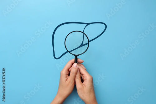 Silhouette of the liver and hands with a magnifying glass. A symbol of the diagnosis and prevention of liver diseases