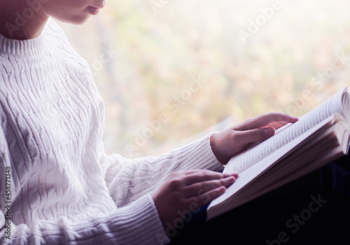 Close view of woman in white woolen sweater holding a book. Free space for your mock up of reading book concept background.