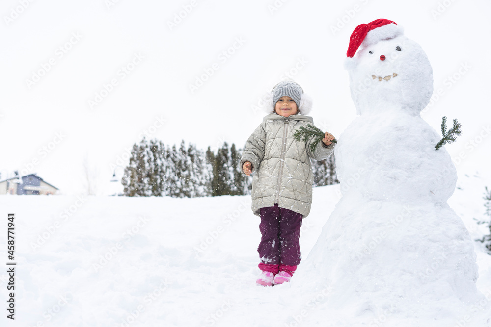 child builds a snowman in the winter in the yard. concept of winter games with snow for children child builds a snowman in the winter in the yard. concept of winter games with snow for children