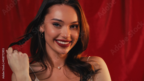 flirty young woman smiling and curling hair on finger on red.