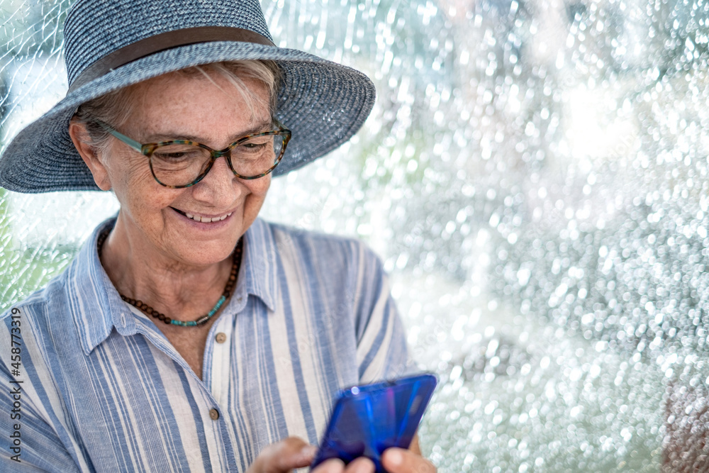 Portrait of senior woman wearing straw hat sitting in shopping mall smiling and using phone Portrait of senior woman wearing straw hat sitting in shopping mall smiling and using phone