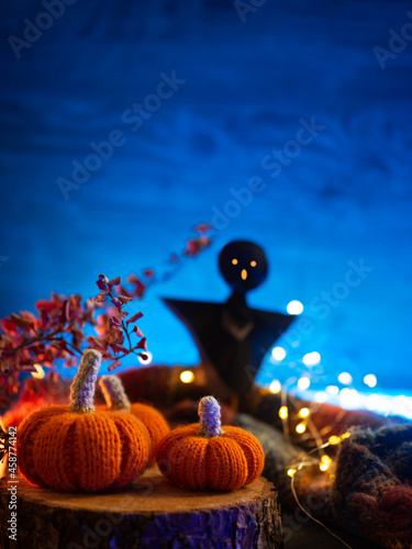Creative Halloween vertical greeting card or banner. Blue backlight, knitted orange pumpkins and a ghost, copy space