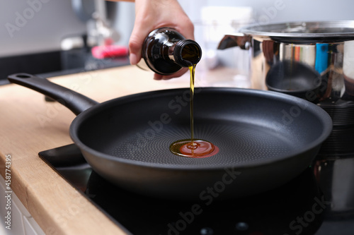 Chef pouring olive oil into frying pan in kitchen closeup photo