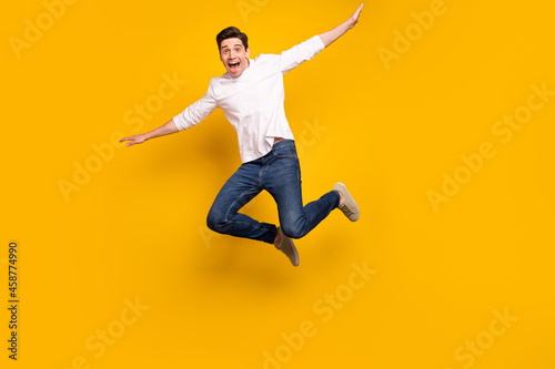 Full body photo of funny brunet young guy jump wear shirt jeans sneakers isolated on yellow background
