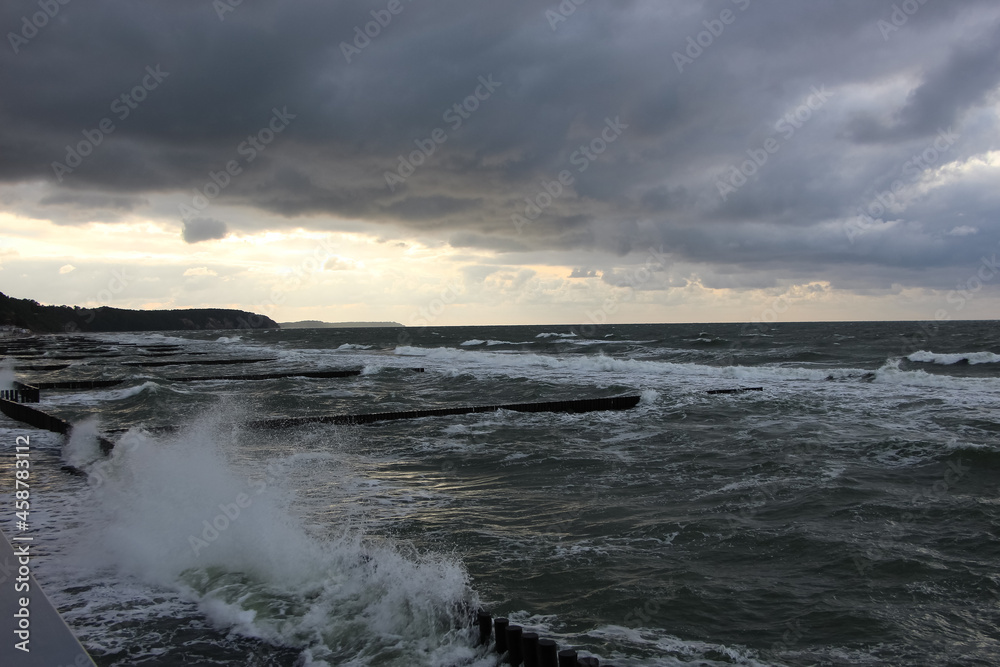 Storm clouds over the Baltic Sea, sunset view of waves and splashes from wooden breakwaters from the high shore