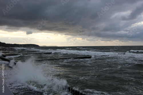 Storm clouds over the Baltic Sea  sunset view of waves and splashes from wooden breakwaters from the high shore